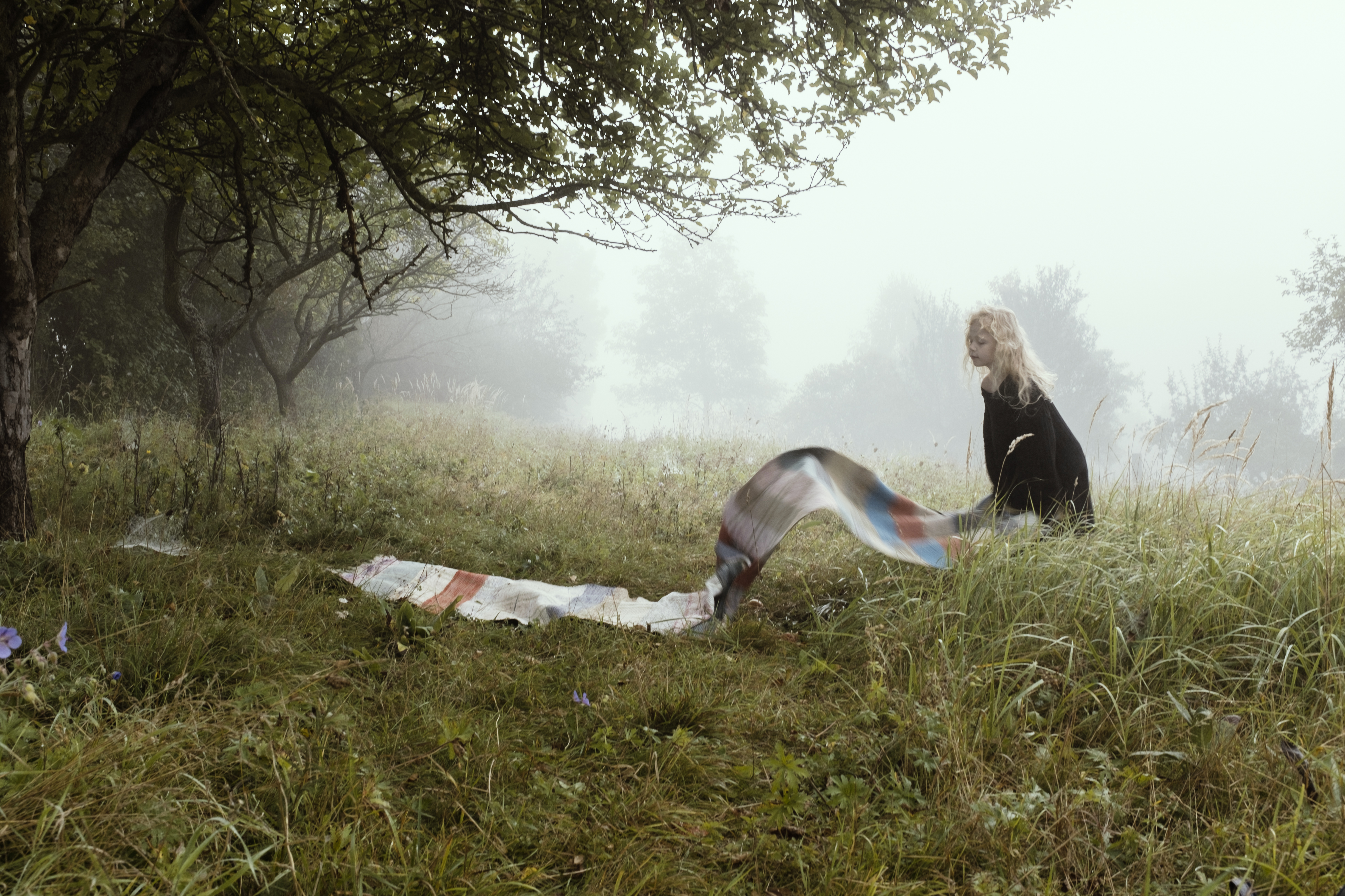 Girl throwing a long colourful rug into grass.